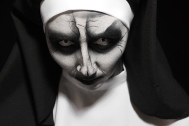 Photo of Portrait of scary devilish nun on black background, closeup. Halloween party look