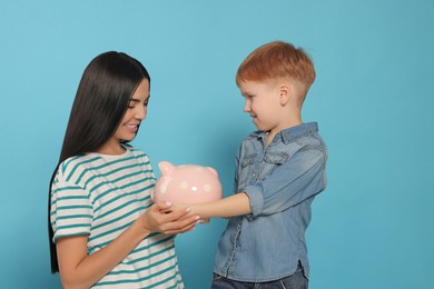 Photo of Mother and her son with ceramic piggy bank on light blue background
