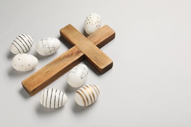 Photo of Wooden cross and painted Easter eggs on light grey background, space for text