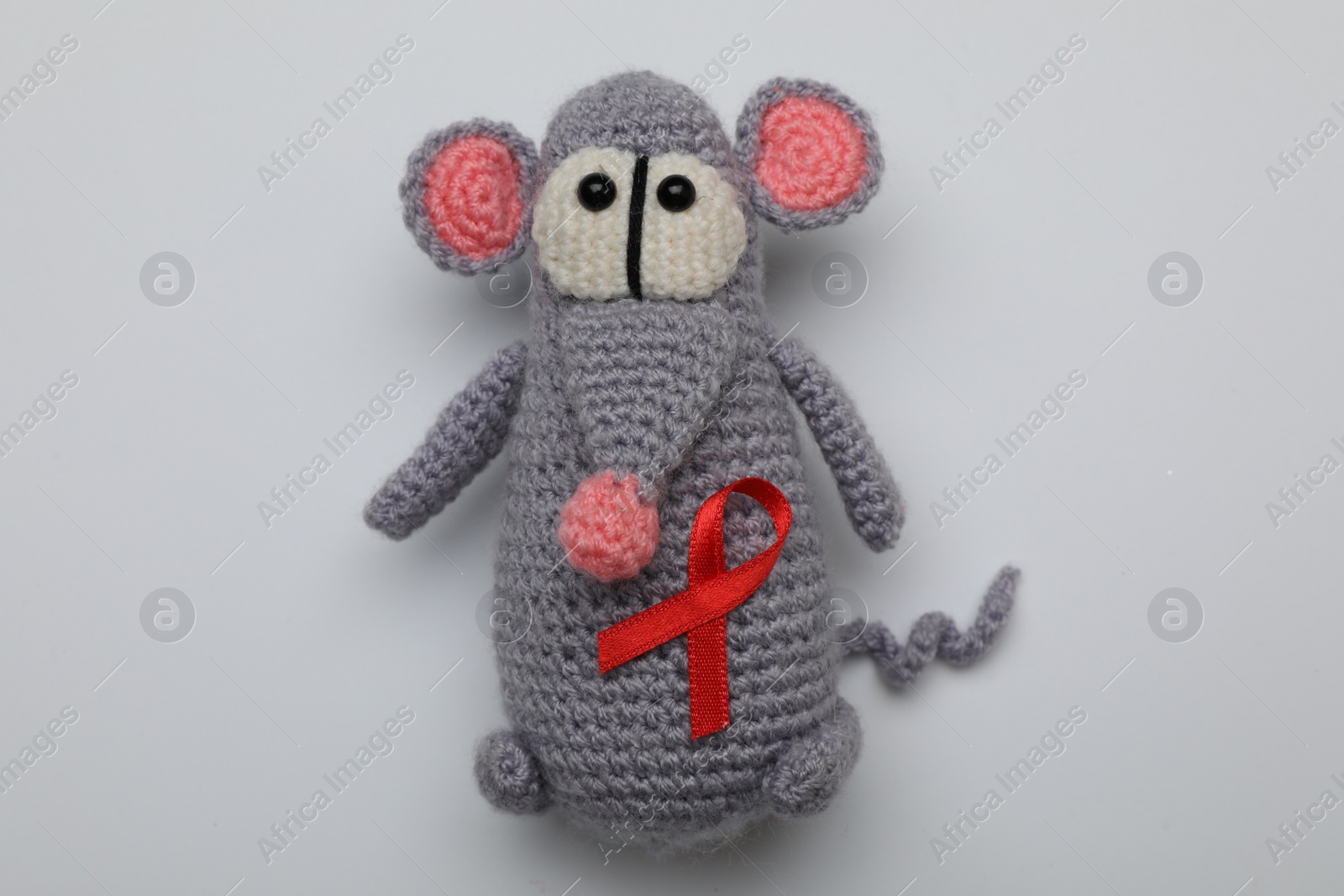 Photo of Cute knitted toy mouse with red ribbon on light grey background, top view. AIDS disease awareness
