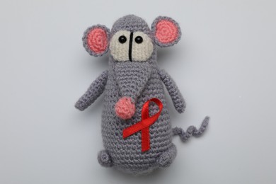 Cute knitted toy mouse with red ribbon on light grey background, top view. AIDS disease awareness