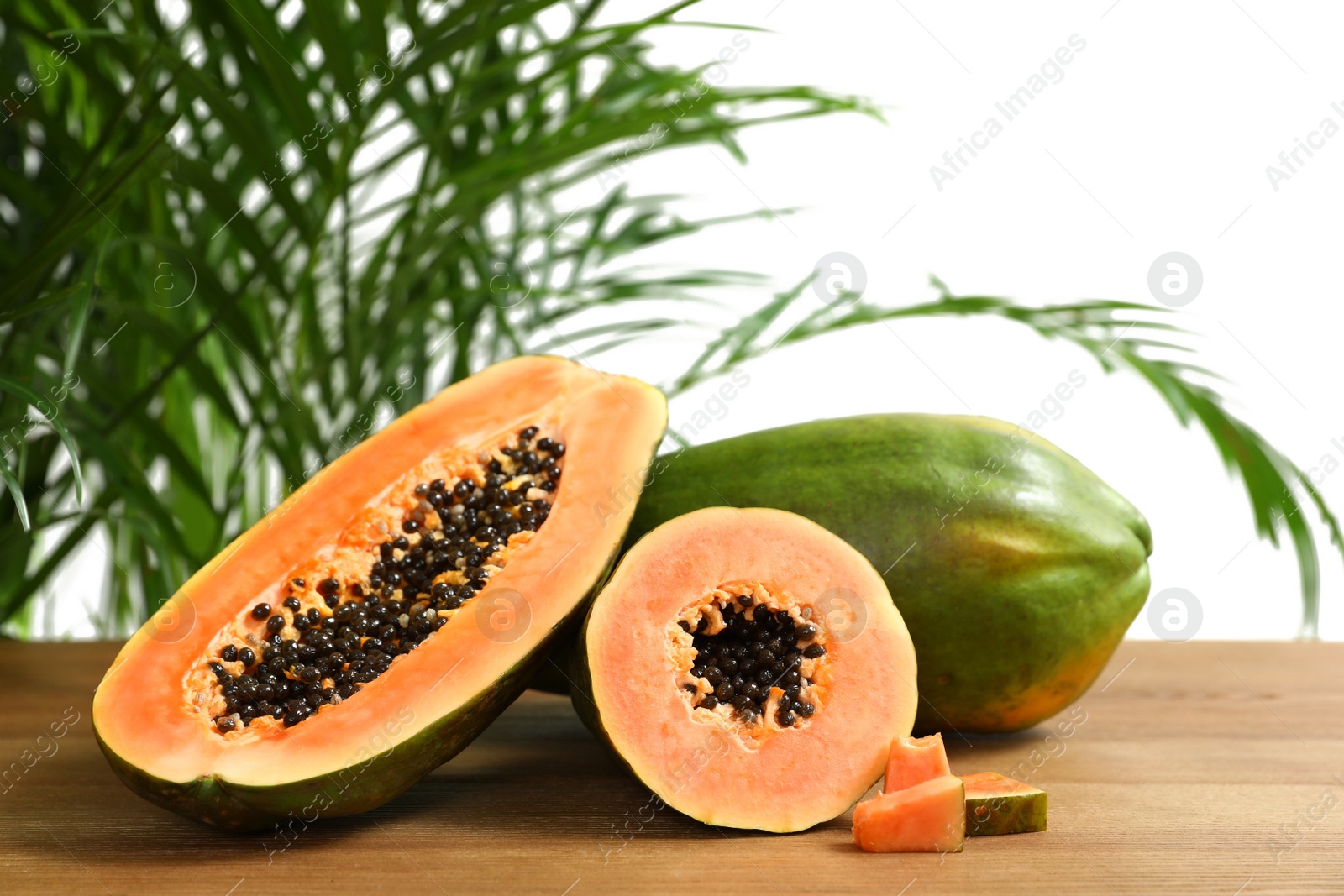 Photo of Fresh juicy cut papayas on wooden table against blurred background, space for text