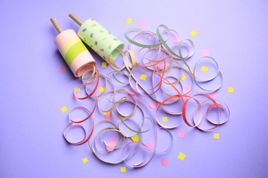 Photo of Beautiful serpentine and confetti bursting out of party poppers on violet background, above view