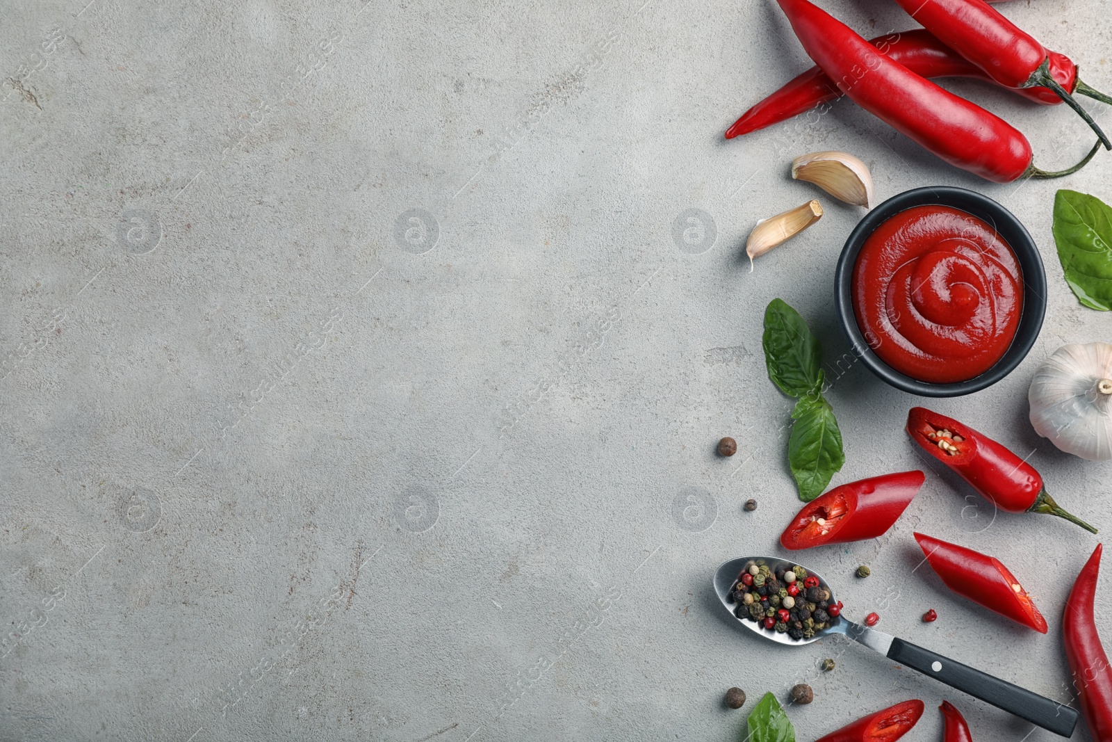 Photo of Flat lay composition with bowl of hot chili sauce and different spices on gray background