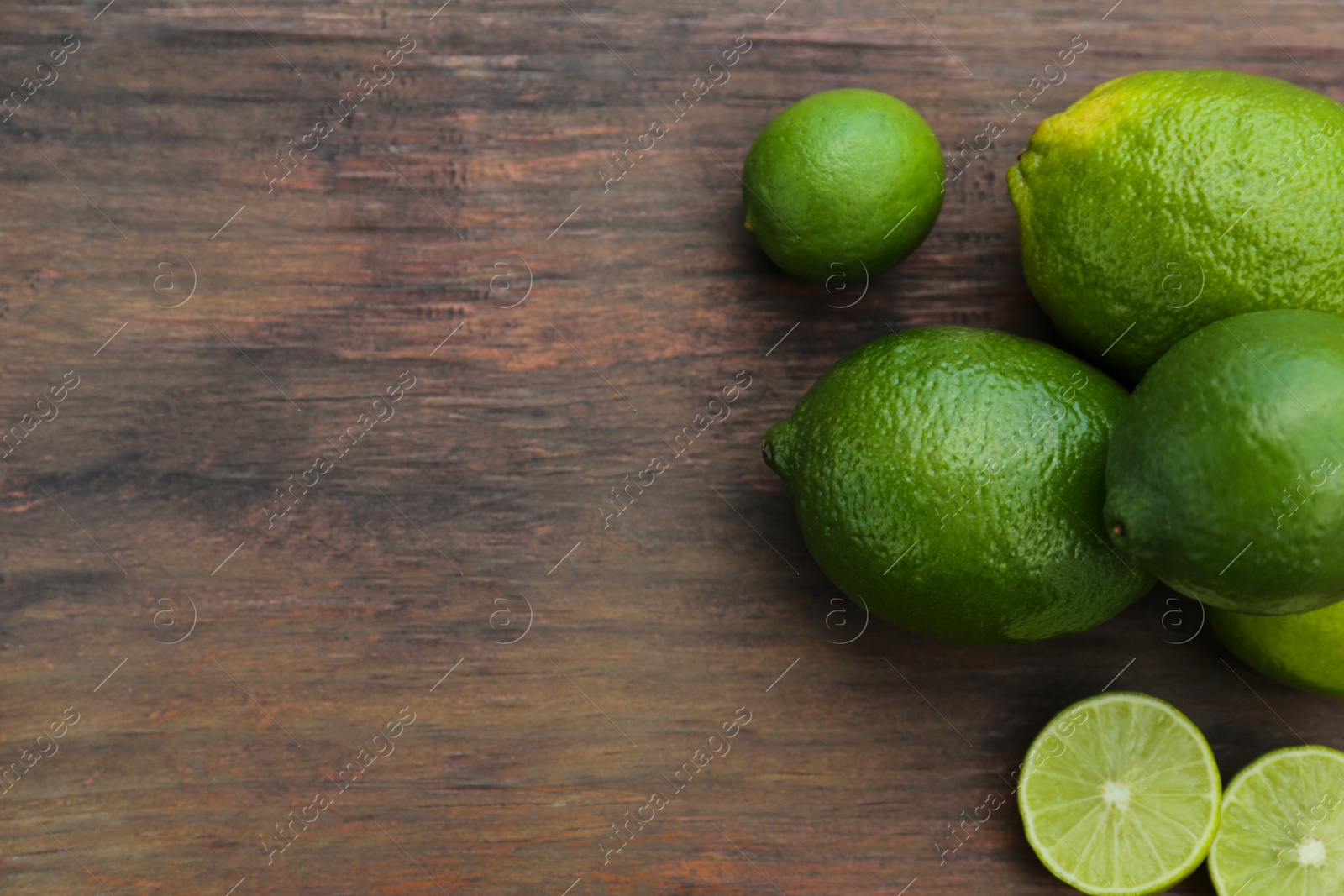 Photo of Whole and cut fresh ripe limes on wooden table, flat lay. Space for text