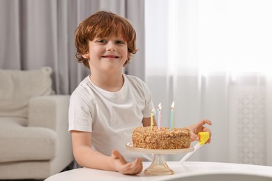 Birthday celebration. Cute boy with party blower at table with tasty cake indoors