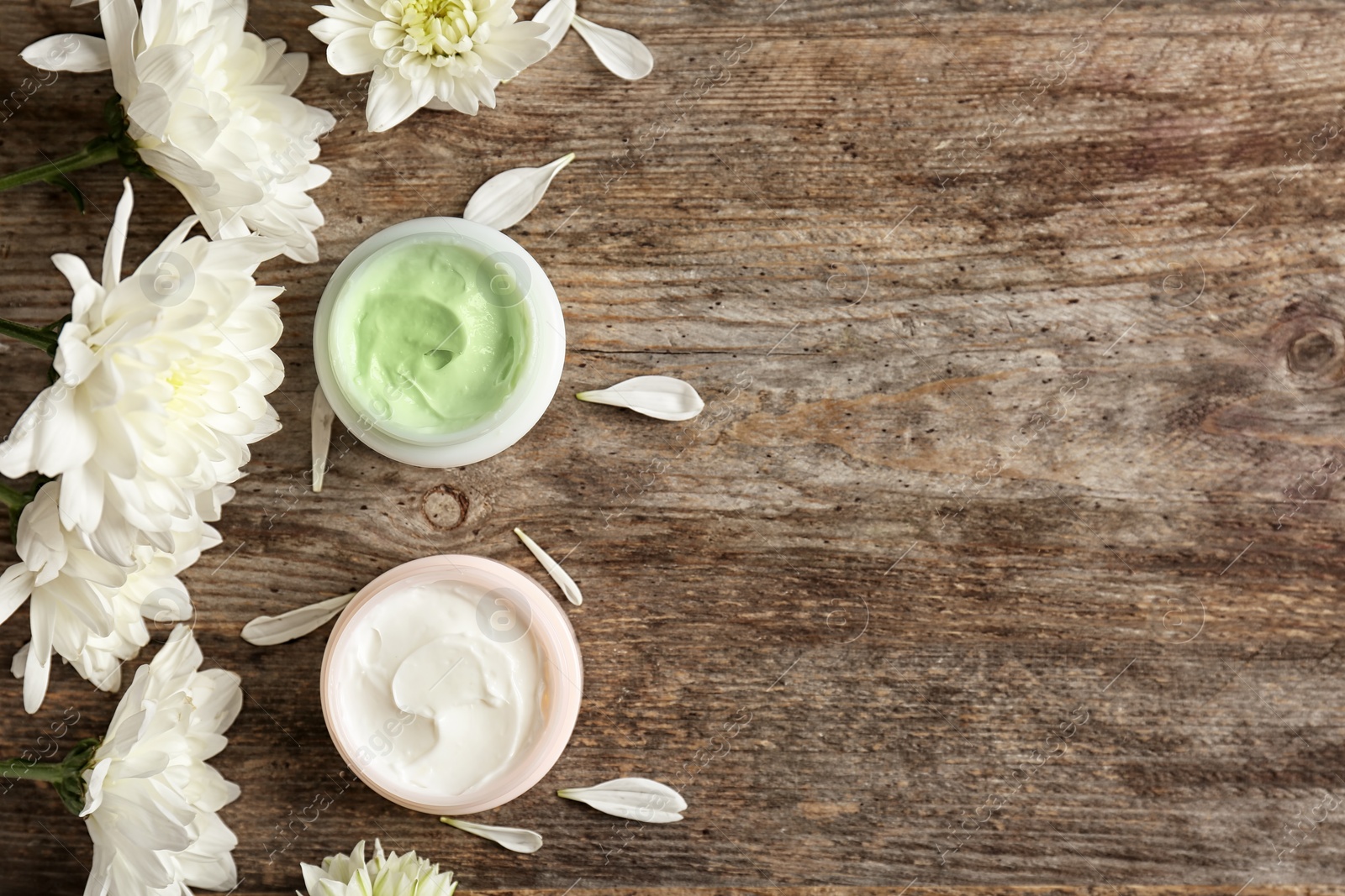 Photo of Beautiful composition with cream and flowers on wooden background, flat lay