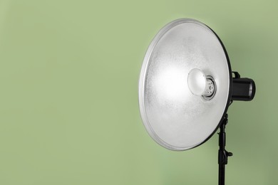 Photo of Professional beauty dish reflector on pale green background, space for text. Photography equipment