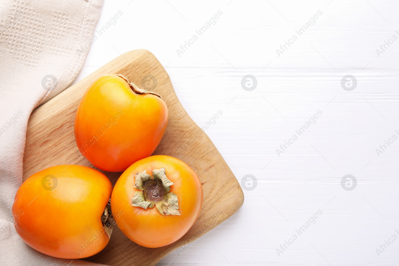 Photo of Board with delicious ripe persimmons on white wooden table, top view. Space for text