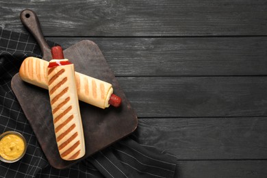 Photo of Delicious french hot dogs and dip sauce on black wooden table, flat lay. Space for text