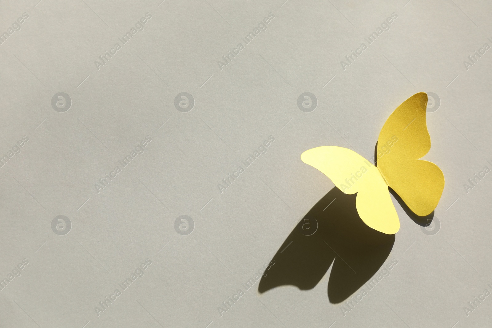 Photo of Yellow paper butterfly on light grey background, above view. Space for text