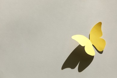 Photo of Yellow paper butterfly on light grey background, above view. Space for text