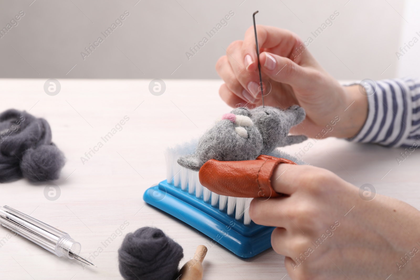 Photo of Woman felting toy cat from wool at light wooden table, closeup