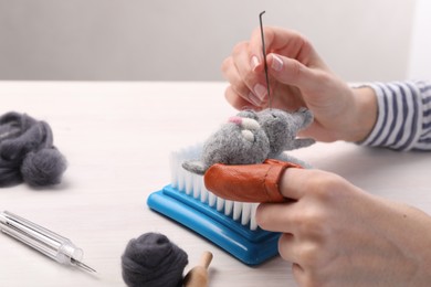 Photo of Woman felting toy cat from wool at light wooden table, closeup