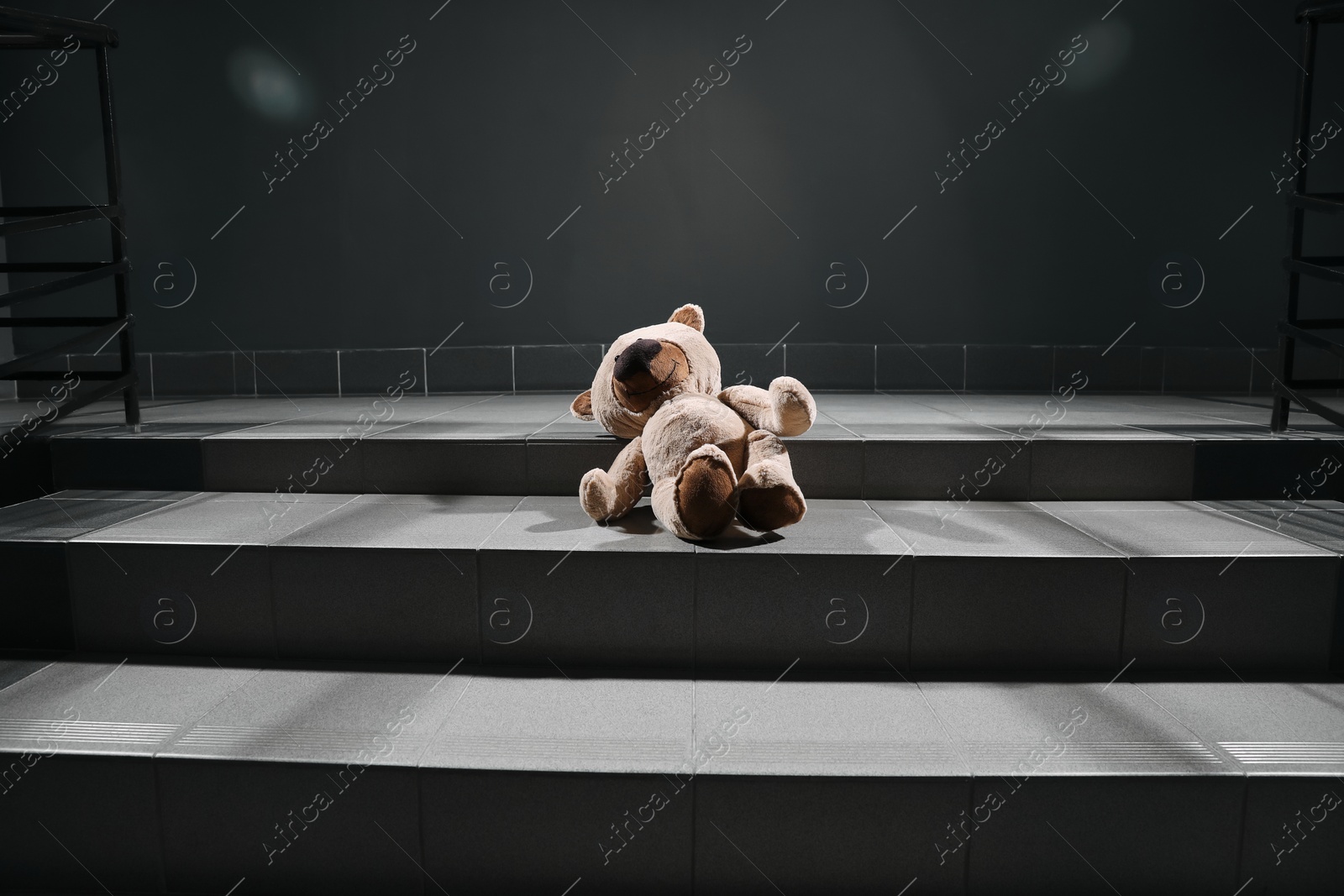 Photo of Lonely teddy bear on grey stairs indoors