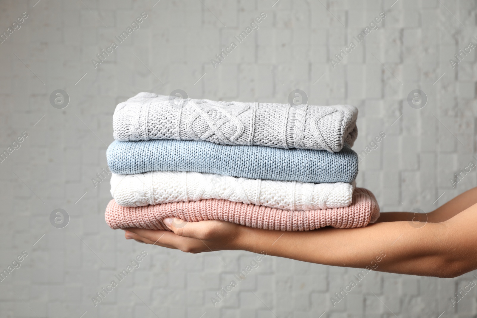 Photo of Woman holding stack of folded warm knitted sweaters against brick wall