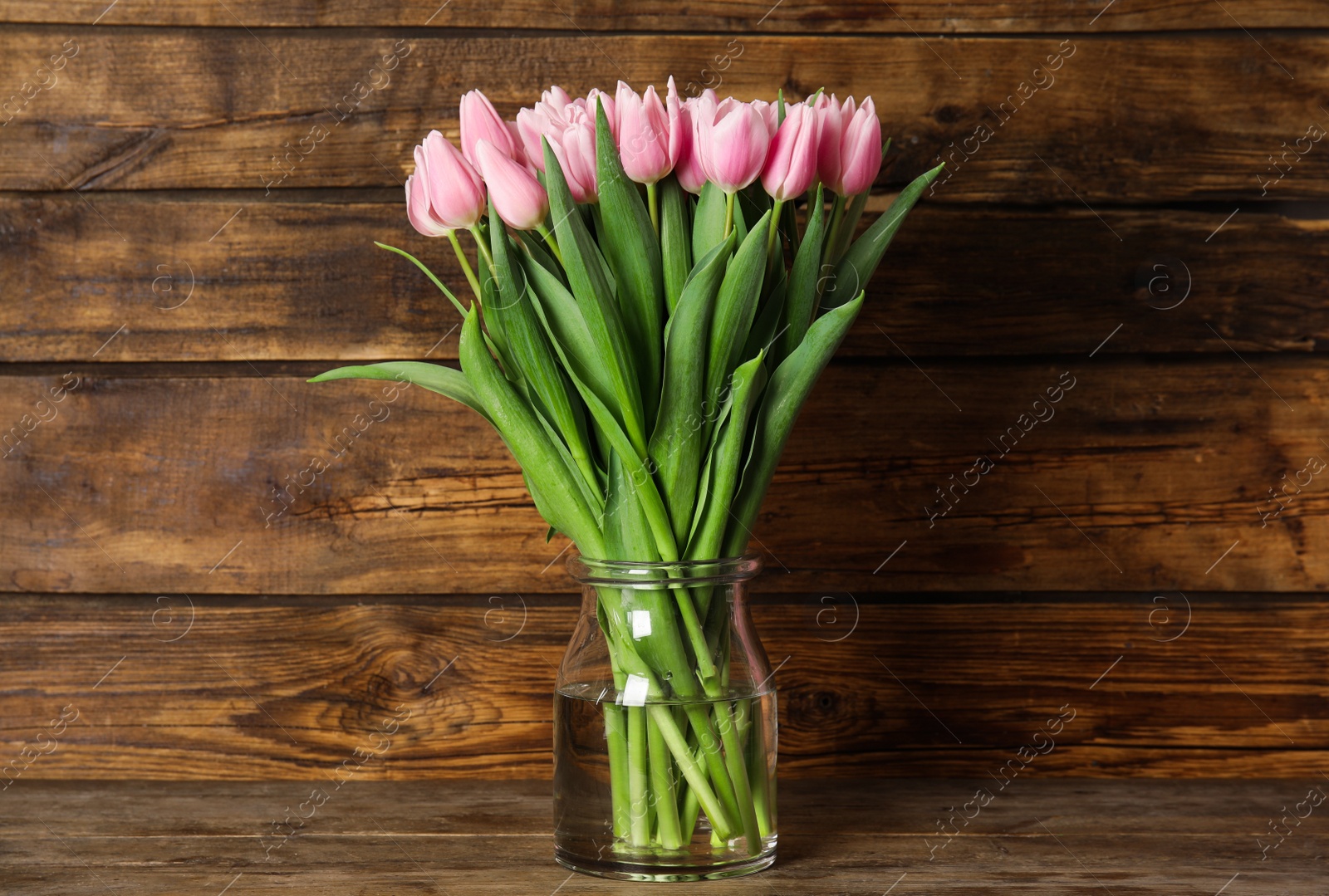 Photo of Beautiful pink spring tulips in vase on wooden table