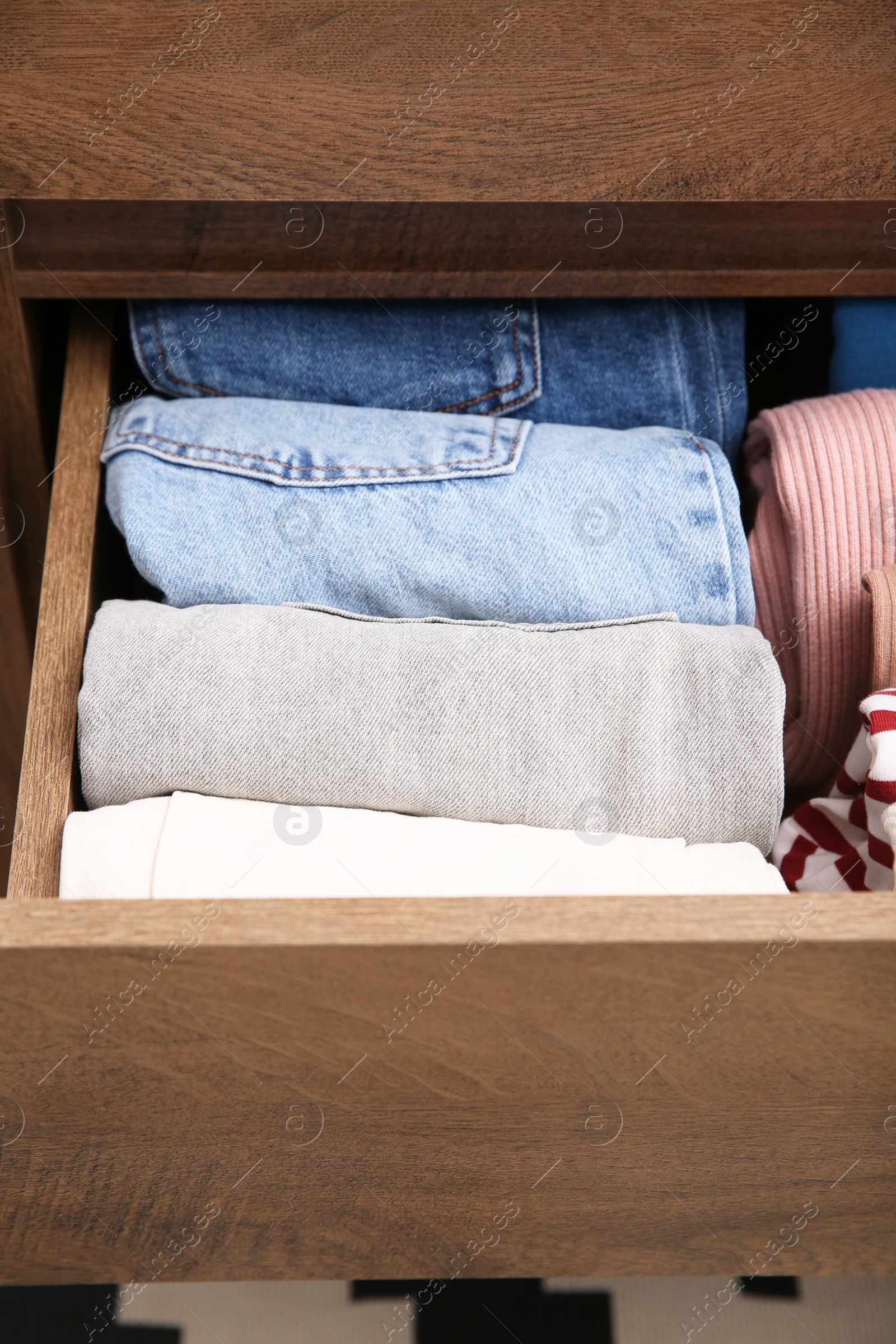 Photo of Open drawer with folded clothes indoors, closeup. Vertical storage