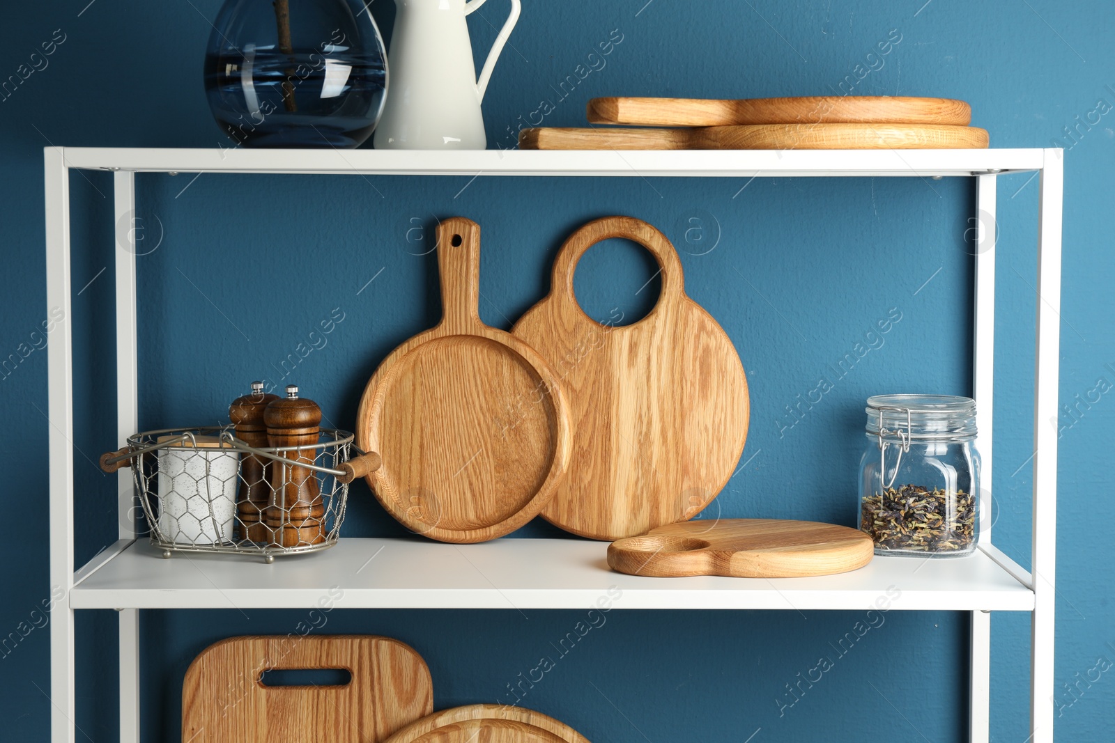 Photo of Wooden cutting boards, kitchen utensils and dry tea on shelving unit near blue wall