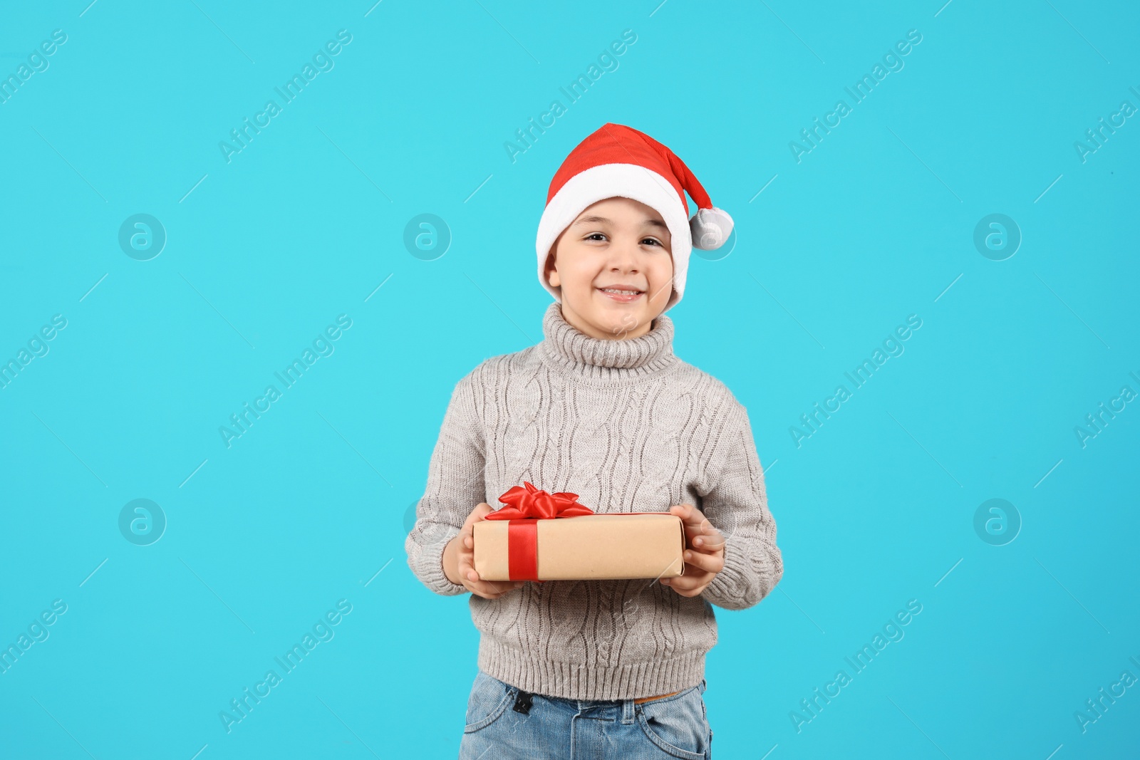 Photo of Cute little child in Santa hat with Christmas gift on color background