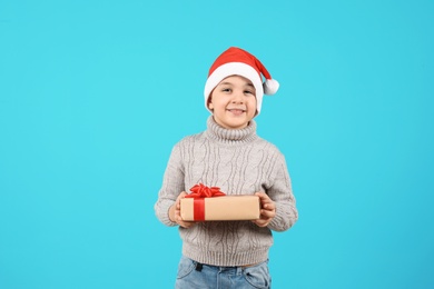 Photo of Cute little child in Santa hat with Christmas gift on color background
