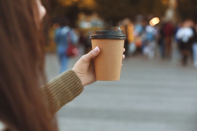 Photo of Woman holding paper takeaway cup on city street, closeup. Coffee to go