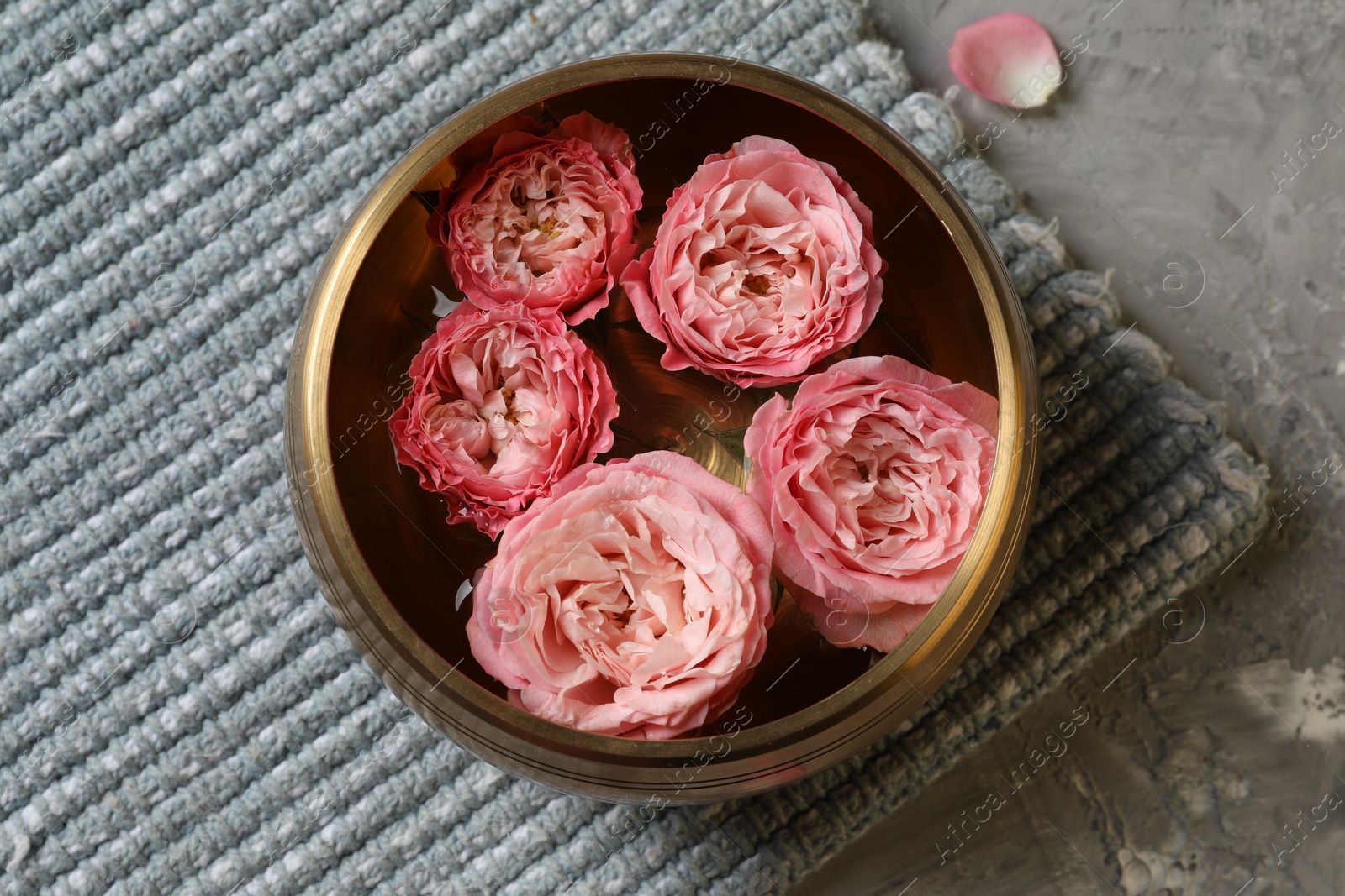 Photo of Tibetan singing bowl with water and beautiful roses on grey textured table, top view