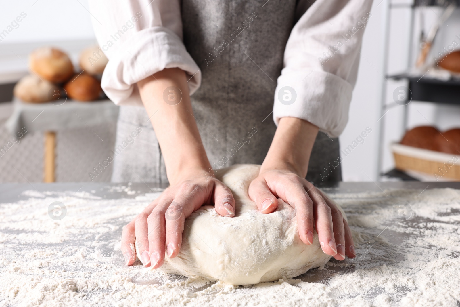 Photo of Woman kneading dough at table in kitchen, closeup