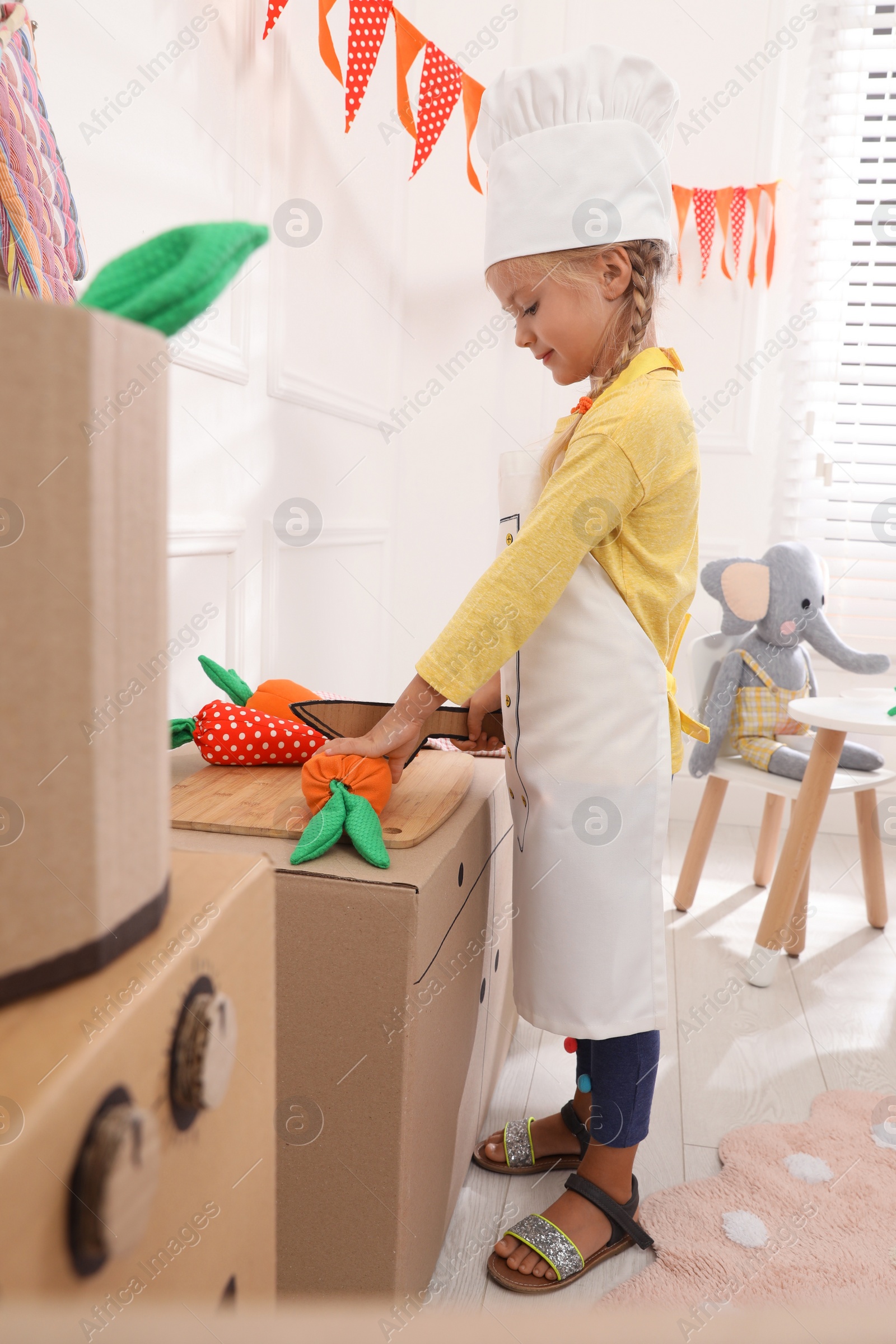 Photo of Little girl playing with toy cardboard kitchen at home