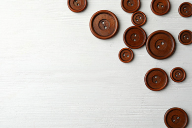 Photo of Many brown sewing buttons on white wooden background, flat lay. Space for text