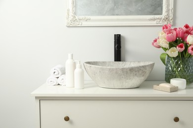 Photo of Vase with beautiful pink tulips and toiletries near sink in bathroom