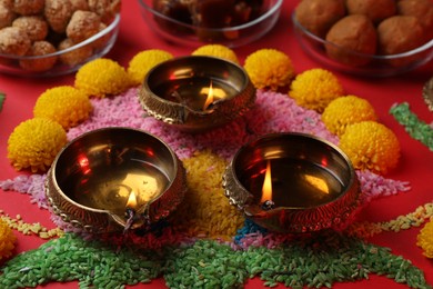 Happy Diwali. Diya lamps, colorful rangoli and flowers on red table, closeup