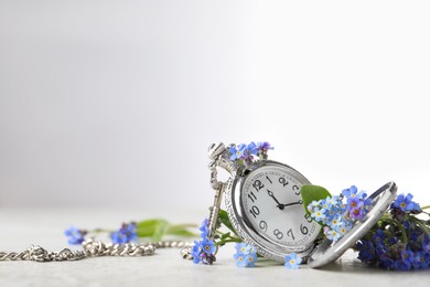 Photo of Beautiful blue forget-me-not flowers with pocket watch on light stone table. Space for text