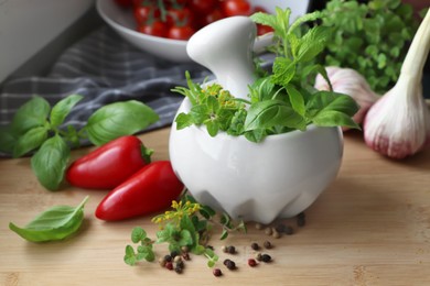Photo of Mortar with fresh herbs near garlic, pepper and cherry tomatoes on wooden table, closeup