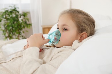 Photo of Little girl using nebulizer for inhalation in bedroom
