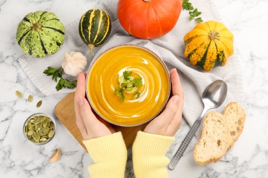 Photo of Woman with bowl of delicious pumpkin soup at white marble table, top view