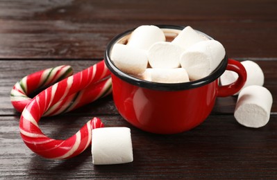 Tasty hot chocolate with marshmallows and candy cane on wooden table, closeup