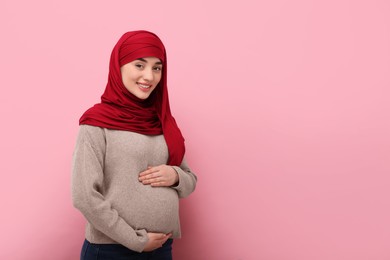 Portrait of pregnant Muslim woman in hijab on pink background, space for text