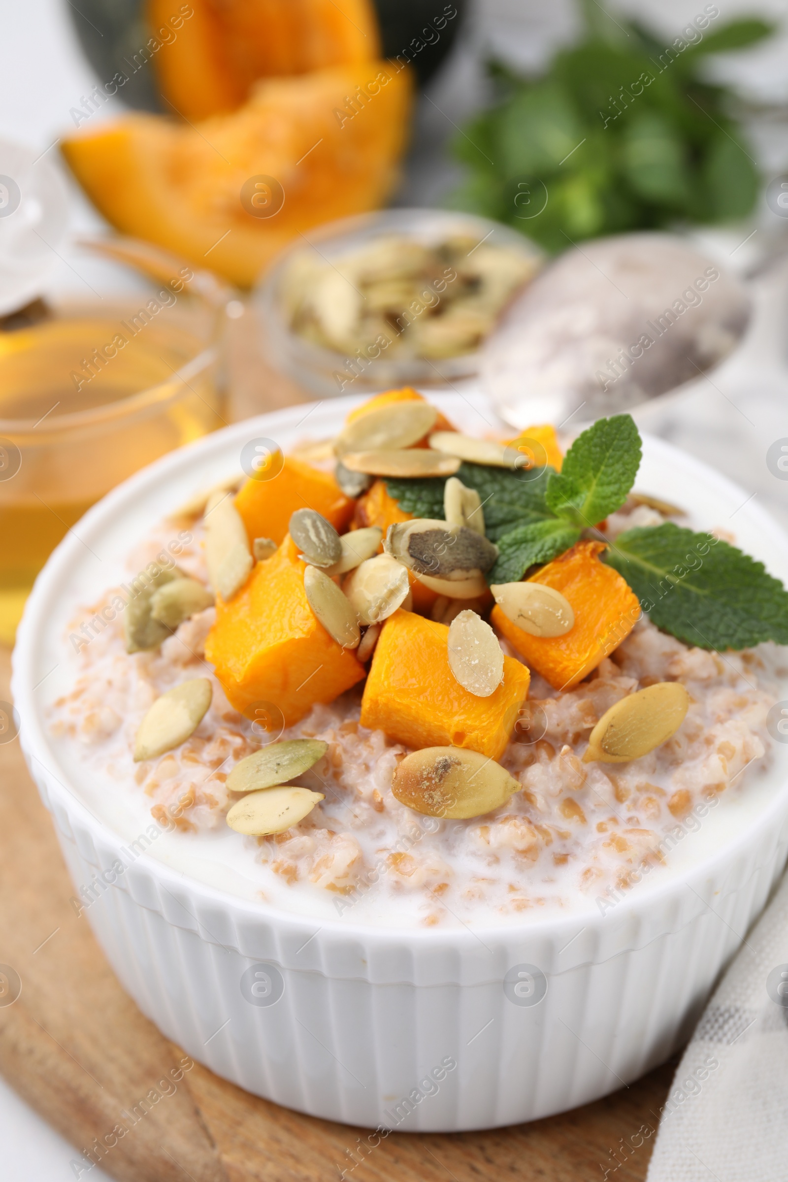 Photo of Tasty wheat porridge with pumpkin and mint in bowl on table, closeup