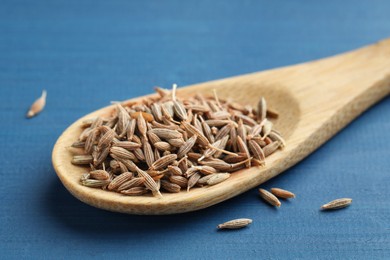 Spoon with caraway seeds on blue wooden table, closeup