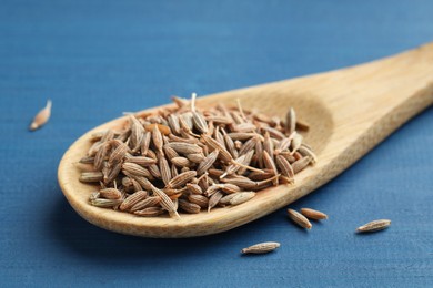 Photo of Spoon with caraway seeds on blue wooden table, closeup