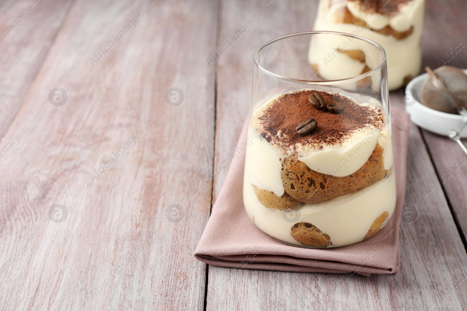 Photo of Delicious tiramisu with coffee beans in glass on wooden table, space for text