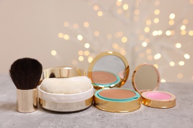 Photo of Bronzer, powder, blusher and brush on grey textured table against blurred lights
