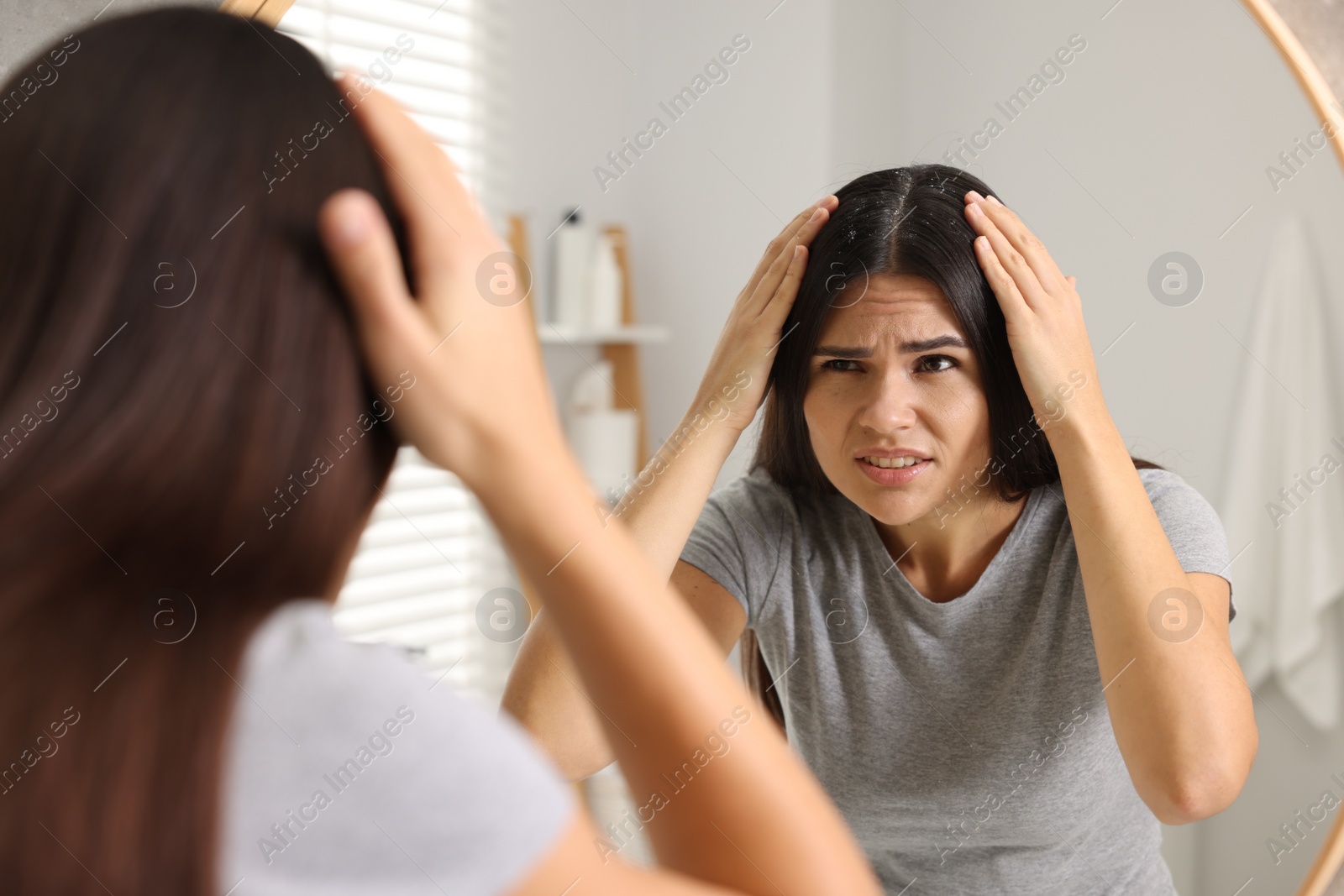 Photo of Emotional woman examining her hair and scalp near mirror in bathroom. Dandruff problem