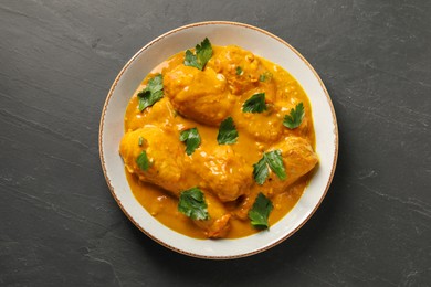 Photo of Tasty chicken curry with parsley on black textured table, top view
