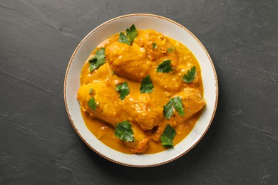 Tasty chicken curry with parsley on black textured table, top view