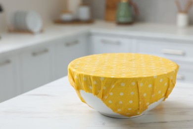 Photo of Bowl covered with beeswax food wrap on white table indoors, closeup. Space for text