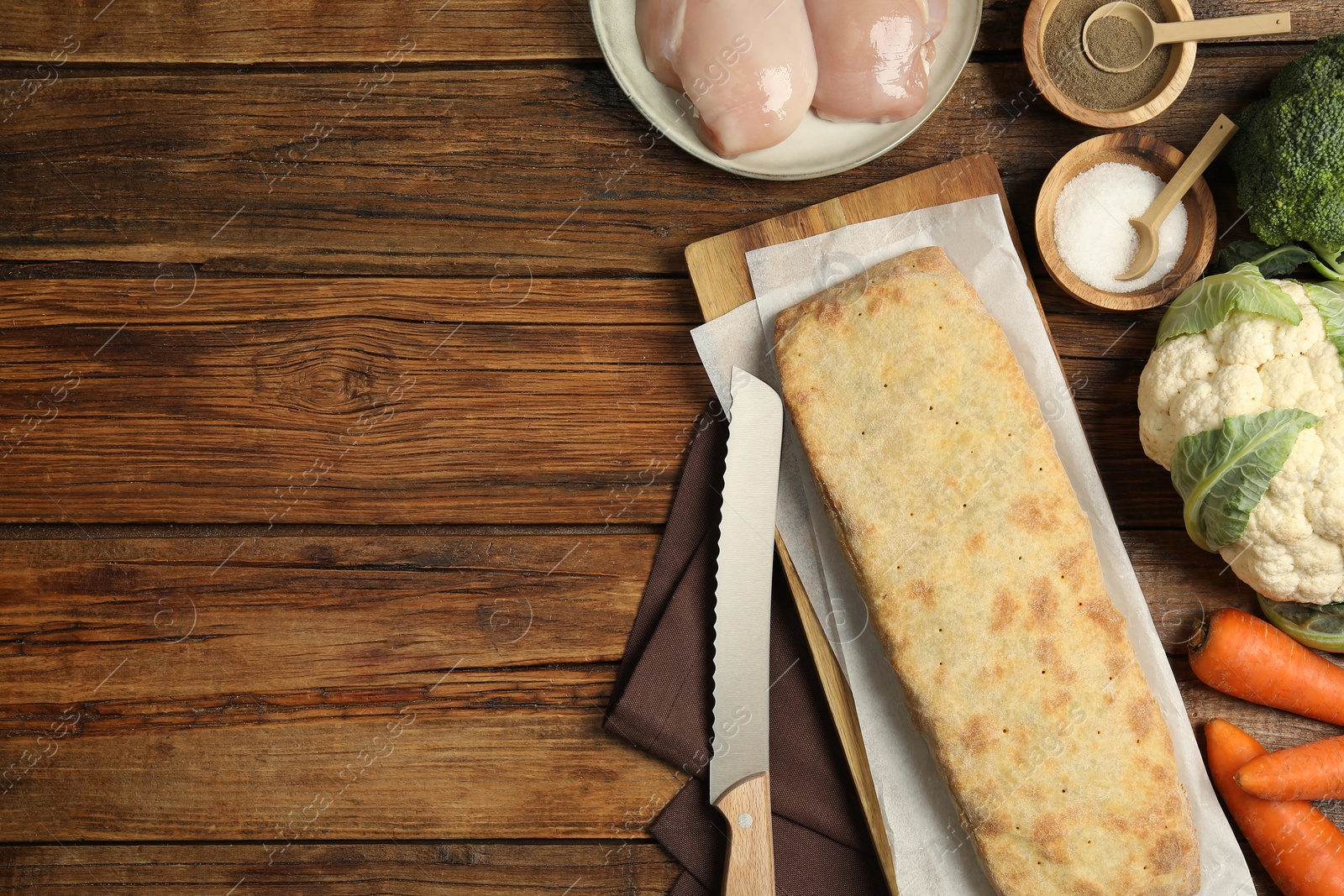 Photo of Delicious strudel with chicken and vegetables on wooden table, flat lay. Space for text