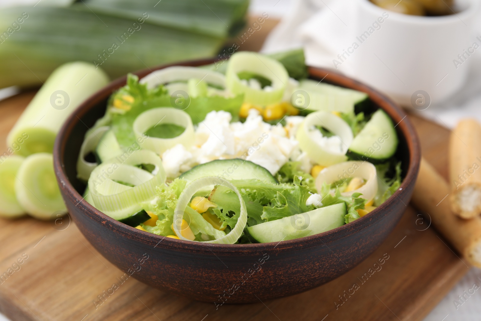 Photo of Bowl of tasty salad with leek and cheese on table, closeup