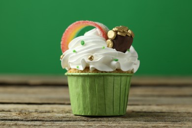 Photo of St. Patrick's day party. Tasty cupcake with sour rainbow belt and pot of gold toppers on wooden table, closeup